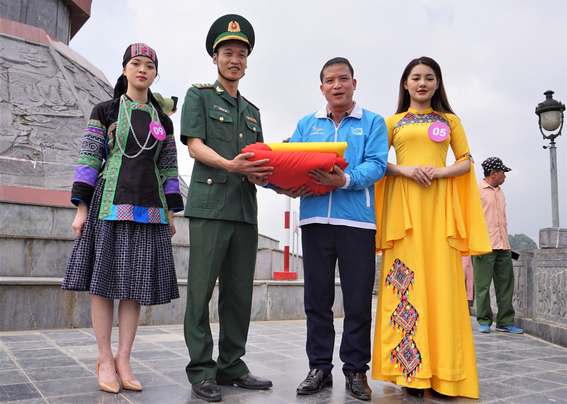 Đồng chí Thèn Văn Quân, phó Bí thư Tỉnh đoàn và 2 thí sinh Người đẹp miền Cao nguyên đá trao lá quốc kỳ 54m2 tượng trưng cho 54 dân tộc Việt Nam cho Đồn Biên phòng Lũng Cú