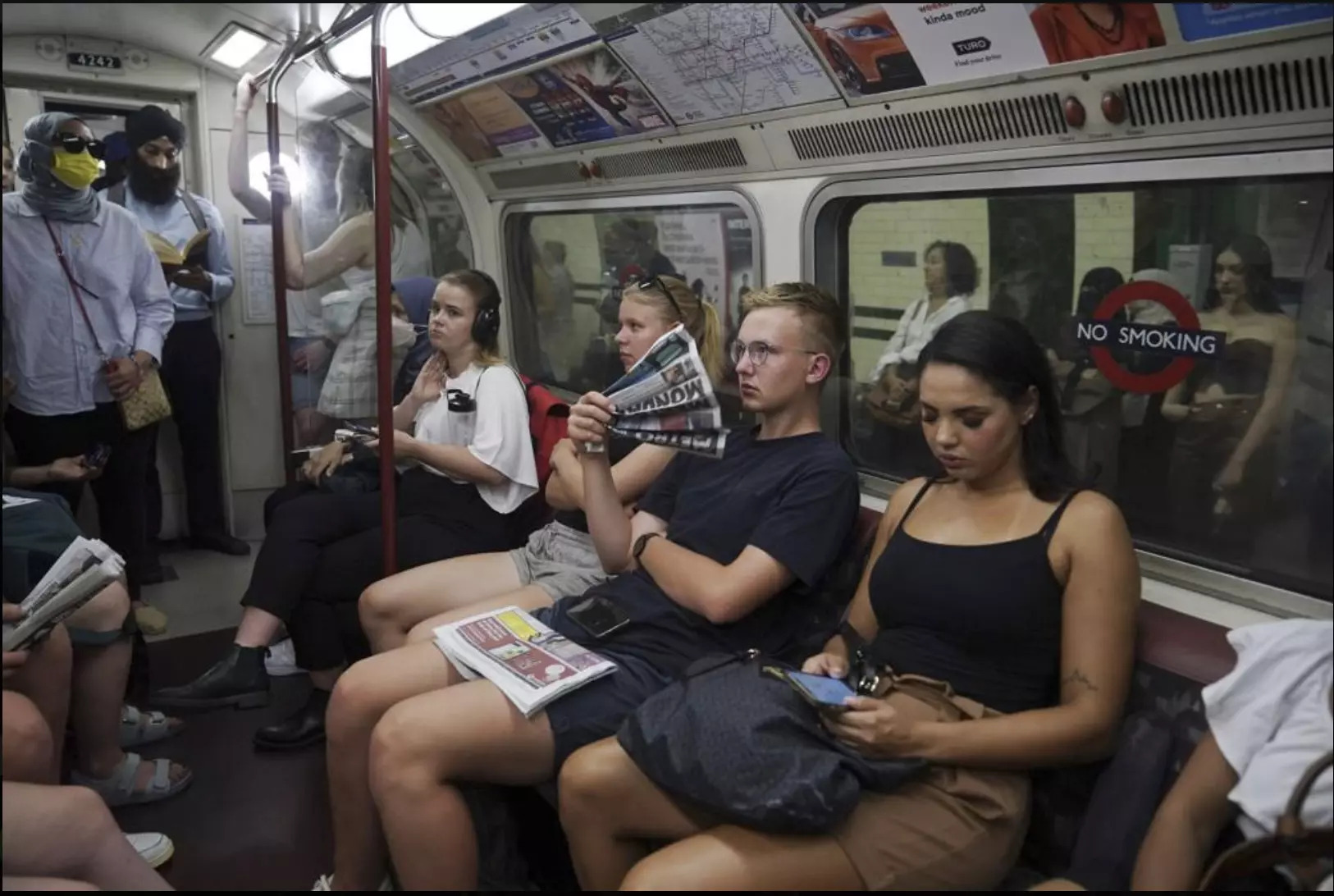 Hành khách đi tàu điện ngầm hạ nhiệt bằng quạt làm từ giấy báo. Ảnh: AP