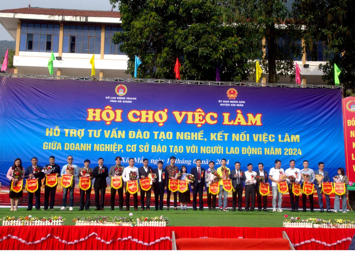 Lãnh đạo Sở Lao động - TB&XH và huyện Xín Mần tặng hoa và Cờ lưu niệm cho các doanh nghiệp tham gia hội chợ.