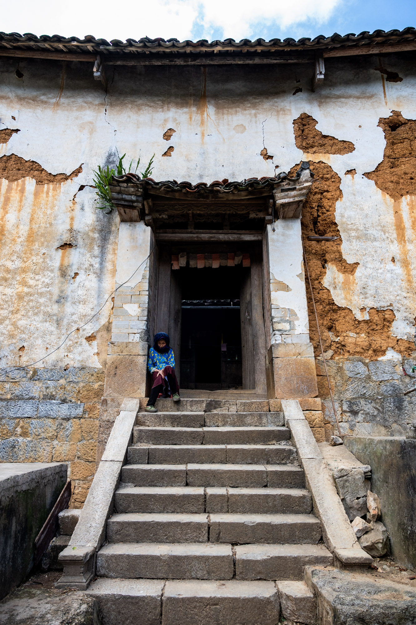 Stone stairs stretch up to the main entrance. Two large square stone blocks were intricately carved, with beautiful patterns at the base of the gate pillars. The main door is made of wood with high door lintels, which is a familiar architectural feature of Mong ethnic people.