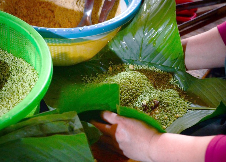 Creating the humped shape requires skilful wrapping. First, glutinous rice is spread evenly on the dong leaf, then seasoned pork belly and mung beans are added. The edges of the leaf are then folded to create the distinctive hump shape. This step requires extreme dexterity, as otherwise, the cake will be unbalanced and unattractive. Finally, it’s tied with the bamboo strings.